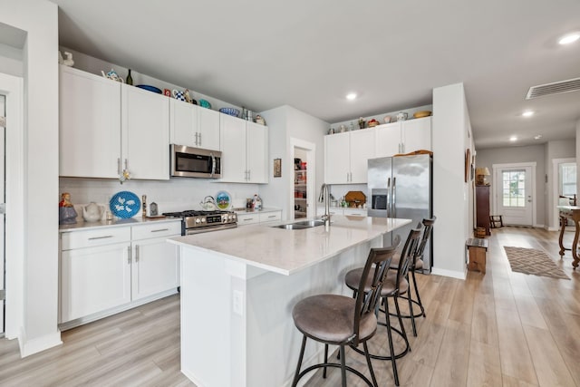 kitchen with a sink, appliances with stainless steel finishes, a breakfast bar area, and light wood finished floors