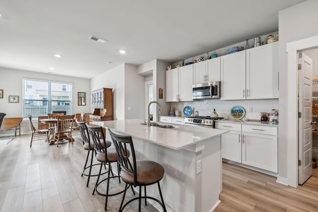 kitchen featuring appliances with stainless steel finishes, a sink, light wood finished floors, a kitchen breakfast bar, and tasteful backsplash