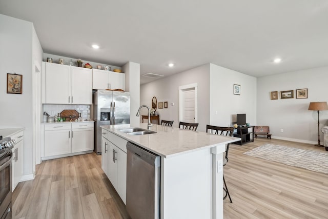 kitchen featuring stainless steel appliances, a sink, light wood-style flooring, and a kitchen bar