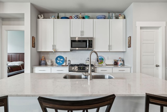 kitchen with a sink, a breakfast bar area, a kitchen island with sink, stainless steel microwave, and tasteful backsplash