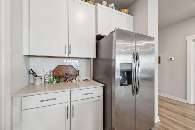 kitchen with white cabinetry, baseboards, decorative backsplash, and stainless steel fridge with ice dispenser
