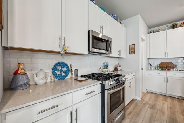 kitchen with decorative backsplash, light wood-type flooring, white cabinetry, light stone counters, and stainless steel appliances