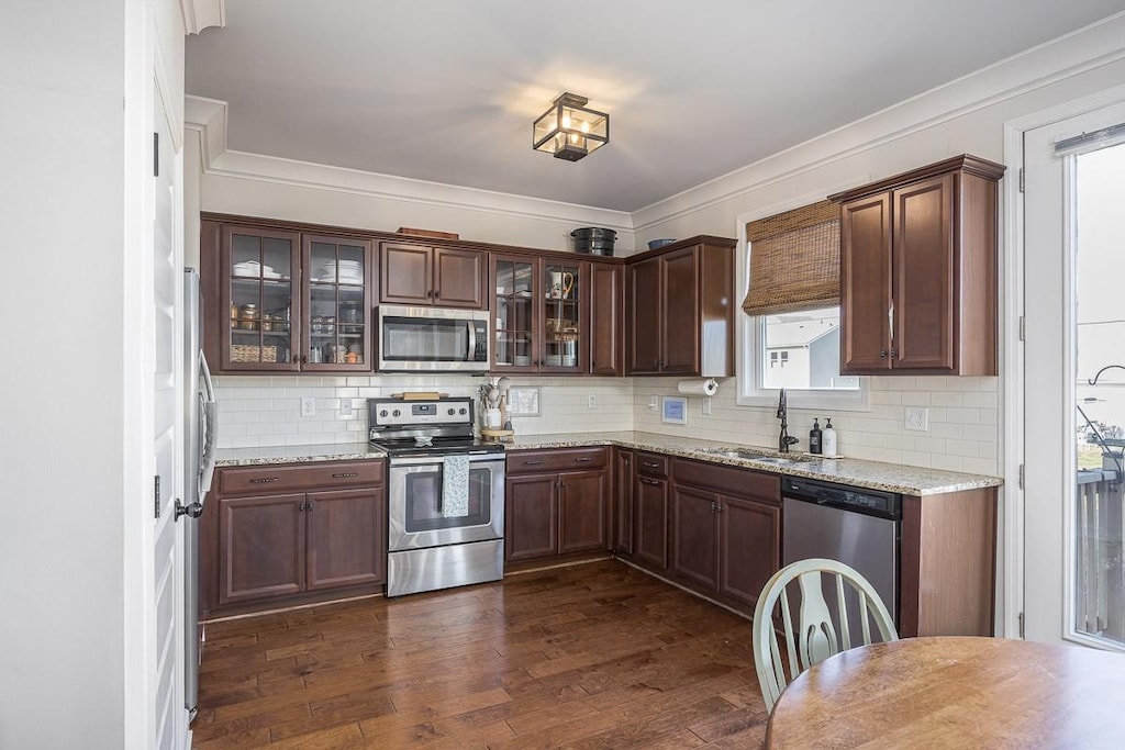 kitchen featuring appliances with stainless steel finishes, a sink, tasteful backsplash, ornamental molding, and glass insert cabinets