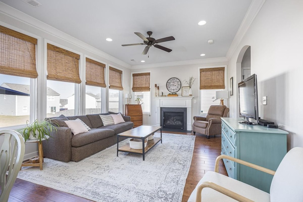 living area with a ceiling fan, dark wood finished floors, and ornamental molding