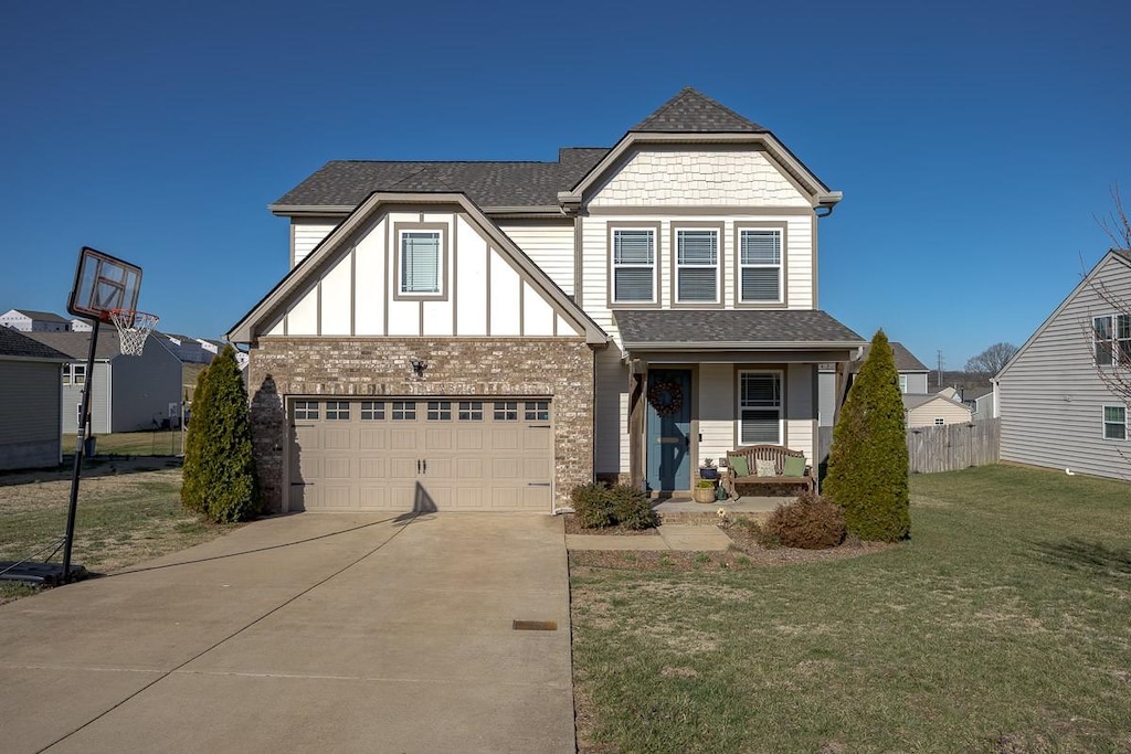tudor home featuring fence, a shingled roof, a front lawn, a porch, and driveway