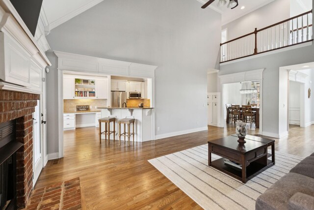 1353 Stewart Creek Rd, Murfreesboro, TN 37129 - living room featuring a brick fireplace, a high ceiling, ornamental molding, wood finished floors, and baseboards
