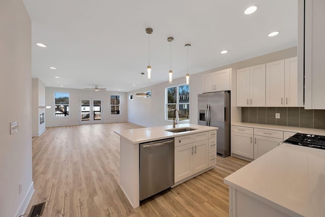 kitchen with appliances with stainless steel finishes, a sink, light wood-style flooring, light countertops, and white cabinets