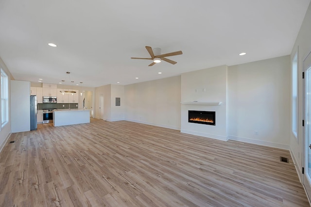 unfurnished living room featuring light wood-type flooring, ceiling fan, recessed lighting, baseboards, and a warm lit fireplace