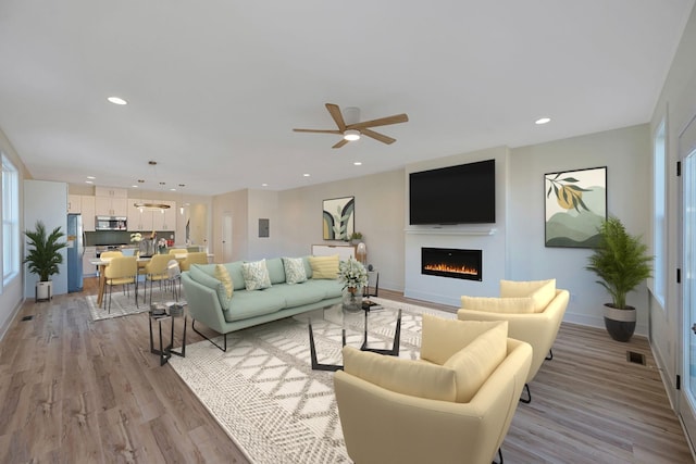 living area featuring light wood-style floors, a lit fireplace, a ceiling fan, baseboards, and recessed lighting