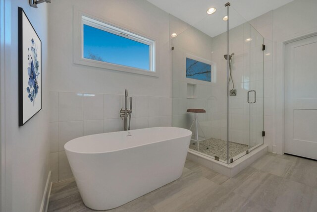 bathroom with a shower stall, a freestanding bath, and tile walls