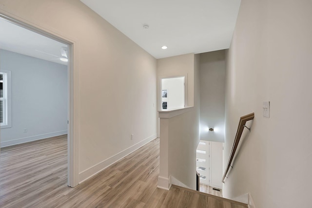 hall with an upstairs landing, light wood-style flooring, and baseboards