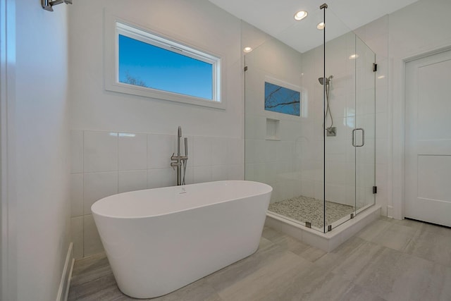 bathroom with a stall shower, a freestanding bath, and tile walls