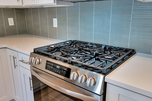 kitchen view of stainless steel gas range oven, decorative backsplash, light countertops, and white cabinets