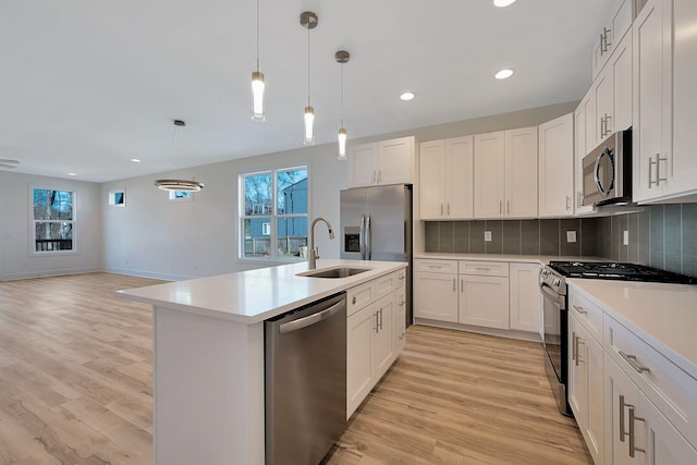 kitchen featuring appliances with stainless steel finishes, a sink, light countertops, tasteful backsplash, and light wood finished floors