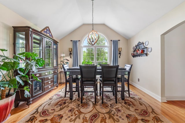 dining area featuring an inviting chandelier, baseboards, vaulted ceiling, and light wood-style flooring