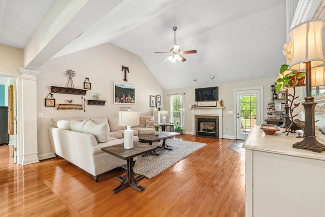 living area with ceiling fan, light wood finished floors, a fireplace, high vaulted ceiling, and decorative columns