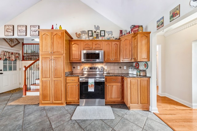 kitchen with appliances with stainless steel finishes, tasteful backsplash, brown cabinets, high vaulted ceiling, and dark stone counters