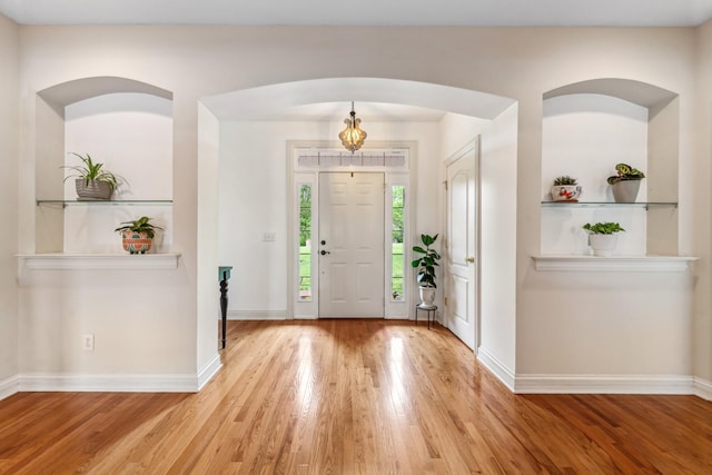 foyer with baseboards, arched walkways, and wood finished floors