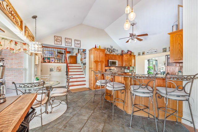 kitchen featuring brown cabinetry, a kitchen breakfast bar, stainless steel microwave, a ceiling fan, and backsplash