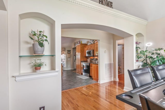 interior space with crown molding, visible vents, light wood-style floors, baseboards, and arched walkways
