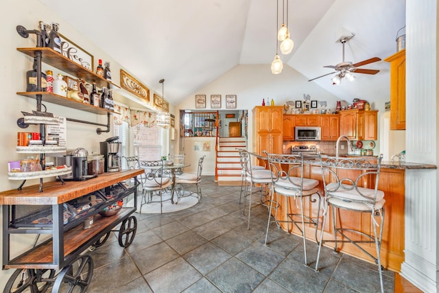 kitchen with brown cabinets, stainless steel appliances, a ceiling fan, backsplash, and vaulted ceiling
