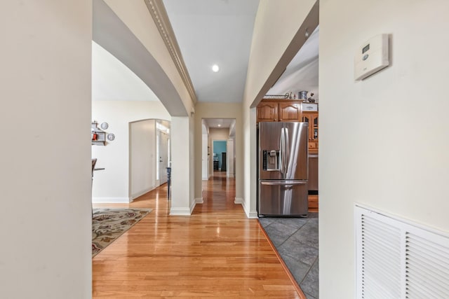 hallway with baseboards, arched walkways, light wood-style flooring, and recessed lighting