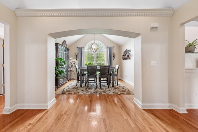 dining space featuring light wood-style floors, arched walkways, baseboards, and vaulted ceiling