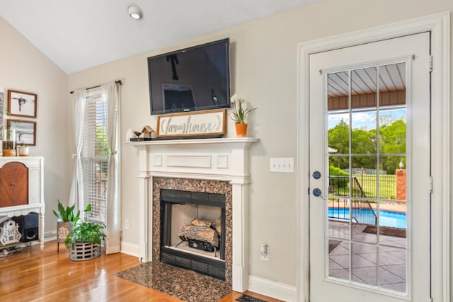 living area with a premium fireplace, baseboards, vaulted ceiling, and wood finished floors
