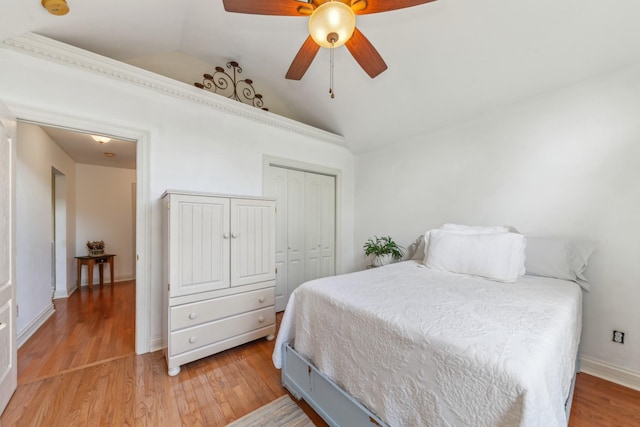 bedroom featuring light wood-style floors, a ceiling fan, baseboards, lofted ceiling, and a closet