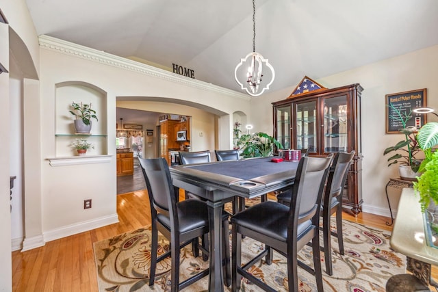 dining room with arched walkways, vaulted ceiling, baseboards, a chandelier, and light wood-style floors