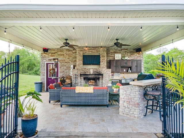 view of patio featuring ceiling fan, an outdoor living space with a fireplace, and a bar