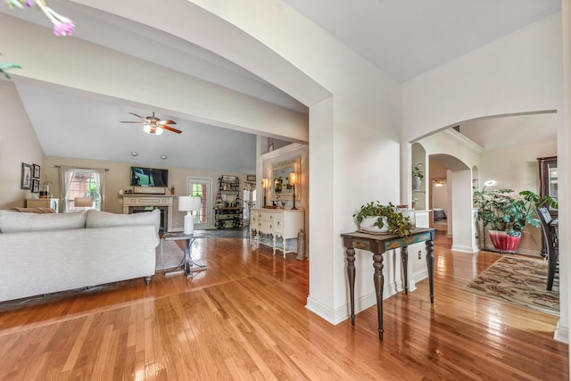 interior space featuring arched walkways, ceiling fan, a fireplace, and light wood-type flooring