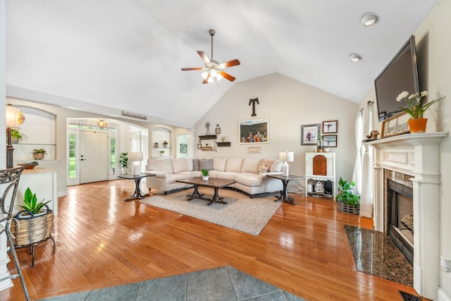 living area featuring wood-type flooring, a fireplace, ceiling fan, arched walkways, and vaulted ceiling