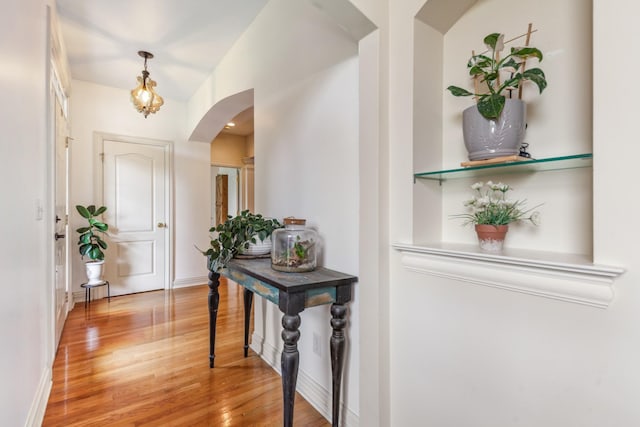 entryway with arched walkways, baseboards, and light wood-style flooring