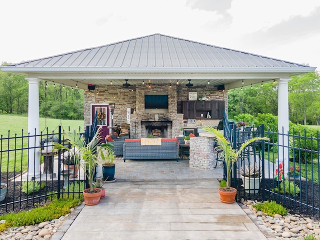view of patio featuring fence, a ceiling fan, an outdoor living space with a fireplace, and a gazebo