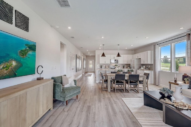 living area with visible vents, recessed lighting, plenty of natural light, and light wood-type flooring