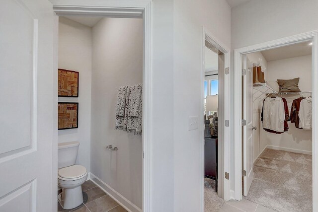 bathroom with baseboards, a walk in closet, tile patterned floors, and toilet