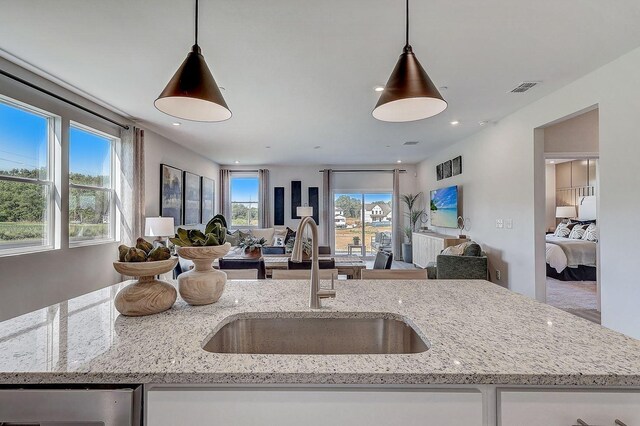 kitchen featuring visible vents, hanging light fixtures, dishwasher, a sink, and open floor plan