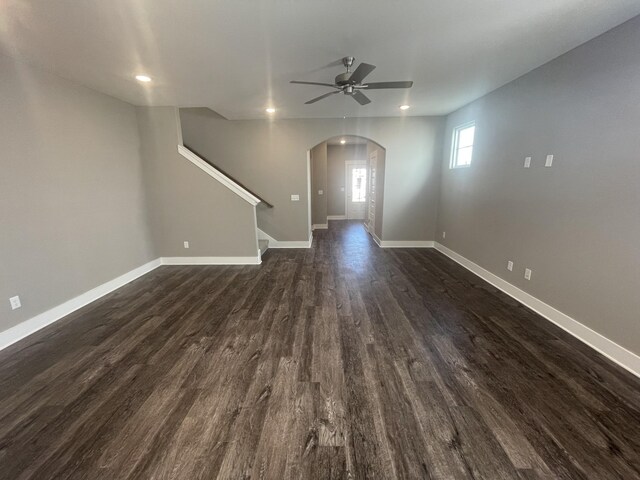 unfurnished living room with a ceiling fan, dark wood-style flooring, arched walkways, baseboards, and recessed lighting