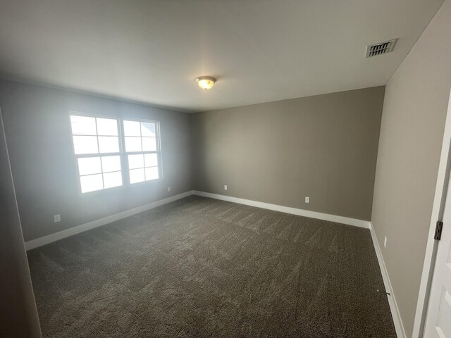 unfurnished room with baseboards, visible vents, and dark colored carpet