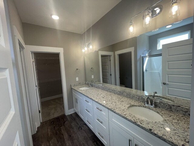 bathroom with double vanity, a stall shower, a sink, and wood finished floors
