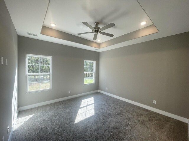 empty room with carpet flooring, a tray ceiling, visible vents, and baseboards