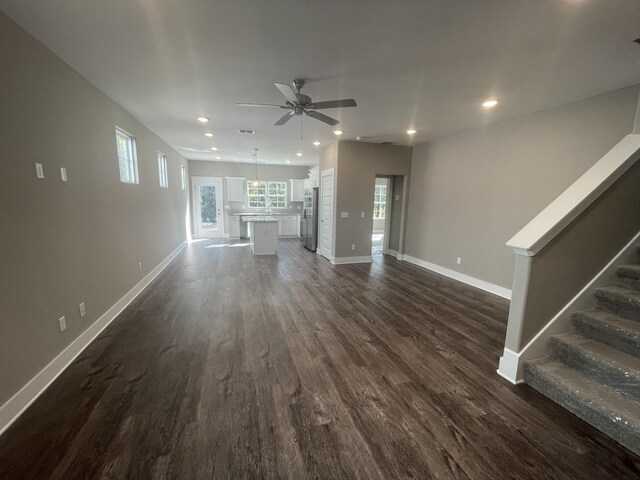 unfurnished living room featuring stairs, a ceiling fan, baseboards, and dark wood finished floors