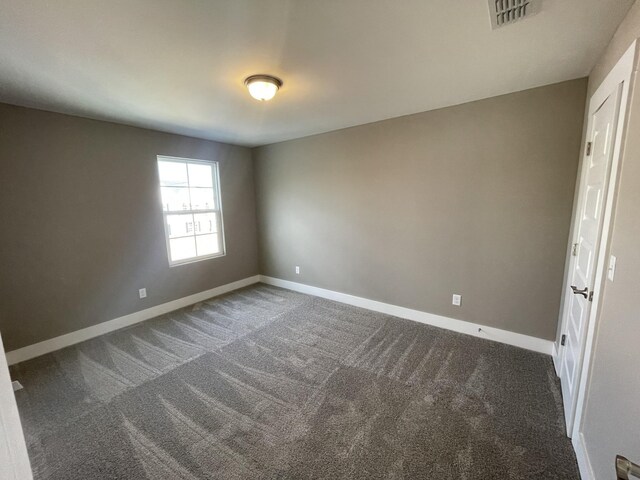 spare room with baseboards, visible vents, and dark carpet