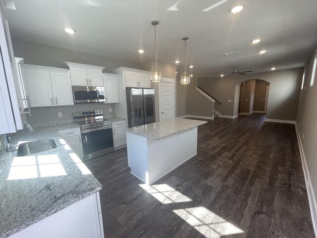 kitchen featuring a sink, a center island, white cabinetry, arched walkways, and appliances with stainless steel finishes