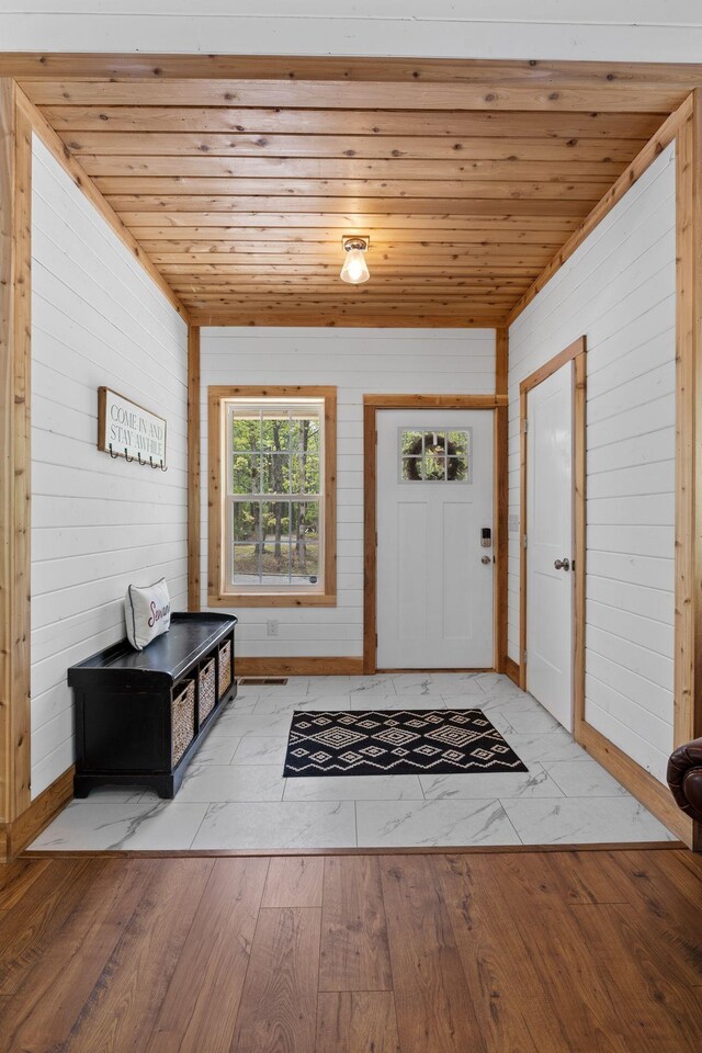 foyer entrance with wood walls, light wood-style flooring, and wooden ceiling