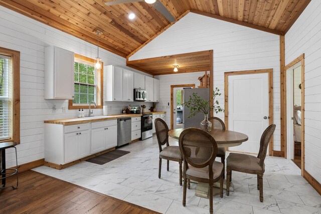 kitchen with butcher block countertops, lofted ceiling, wooden walls, and stainless steel appliances