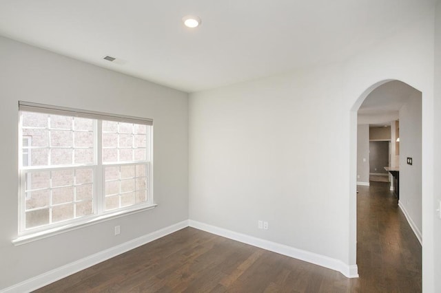 empty room with recessed lighting, arched walkways, baseboards, and dark wood-style floors