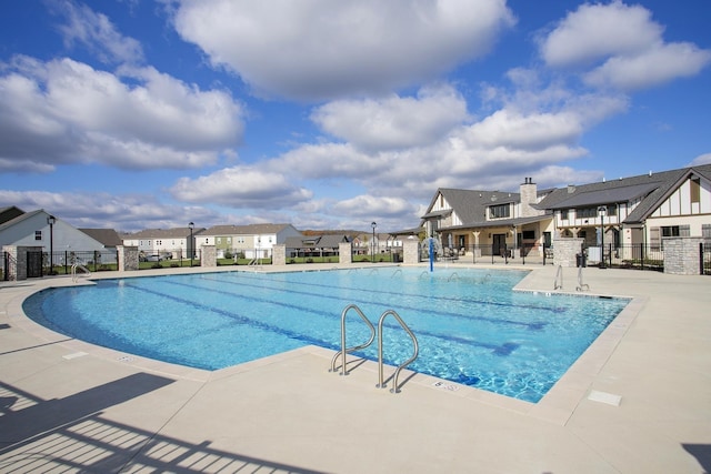 community pool with a patio, fence, and a residential view
