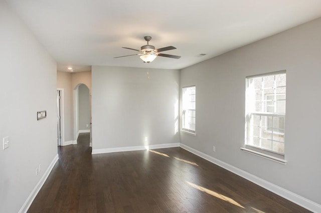 unfurnished room featuring visible vents, baseboards, ceiling fan, dark wood-type flooring, and arched walkways